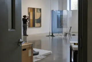 Museum conservator positioning a mid-century abstract painting beside an unfinished contemporary installation.